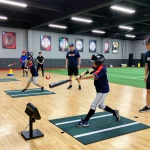 Young athlete practicing hitting at Hitclub training facility with coaches supporting in vibrant indoor environment.